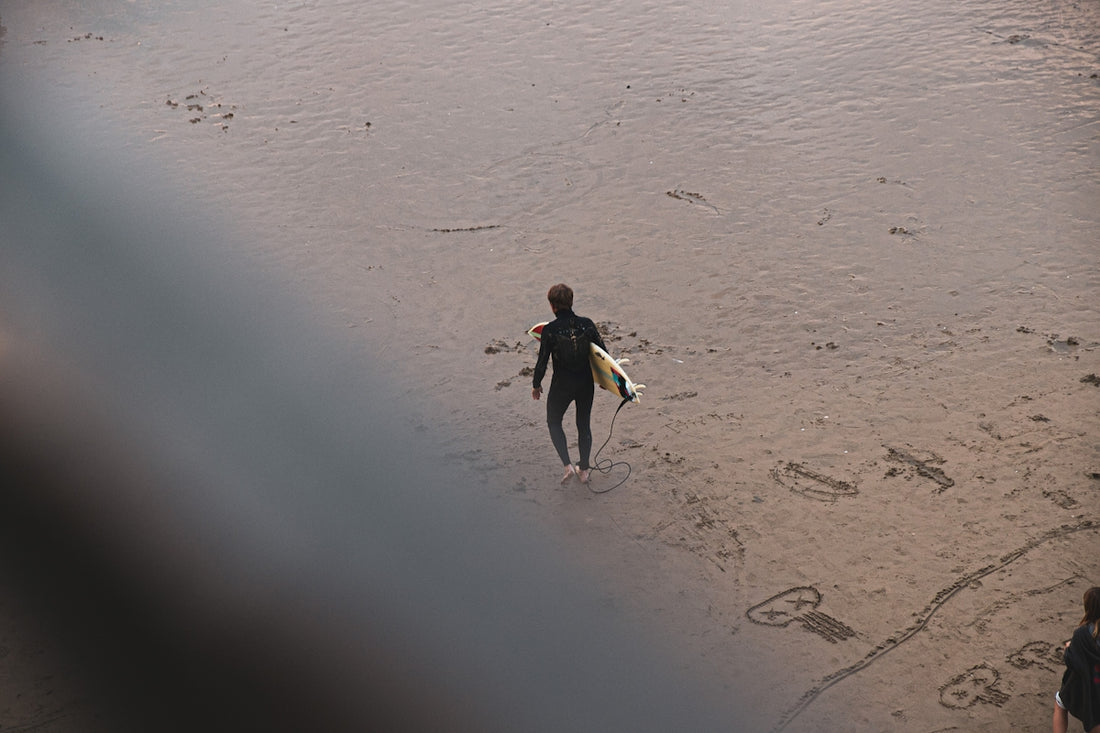 man walking and carrying surfboard on sand during day