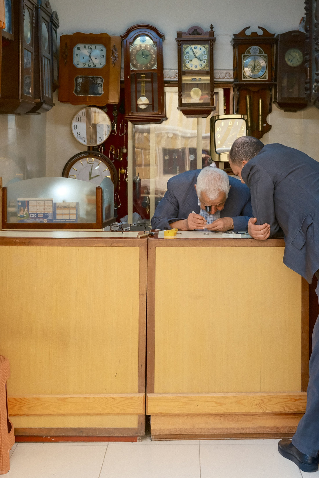 Two men examining a small object in a clock shop.